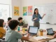 Teacher using an online teacher planner, EMStudio, in a vibrant classroom while students collaborate.